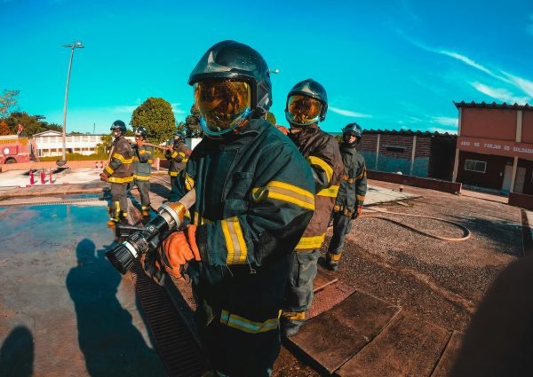 Firefighters in protective suits and helmets manage equipment during training outdoors.